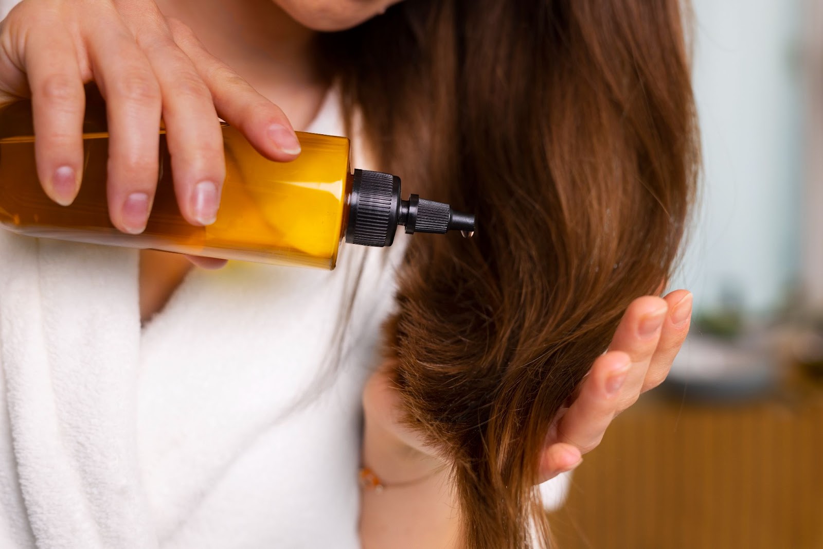 woman applying hair oil to long brown hair